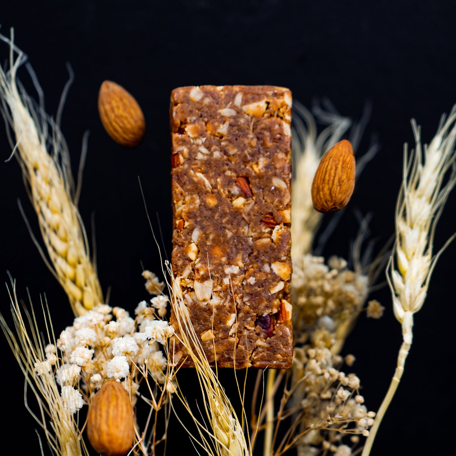 Bar with nuts on a bed of wheat stalks and small white flowers against a black background